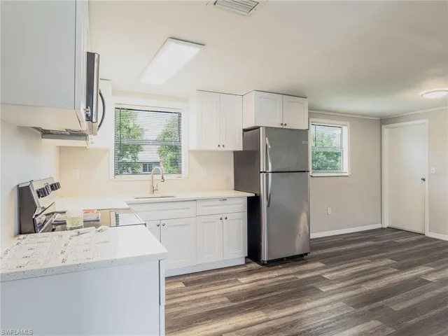 Kitchen featuring white shaker-style cabinetry, light-toned countertops, stainless steel appliances, and wood-finish flooring