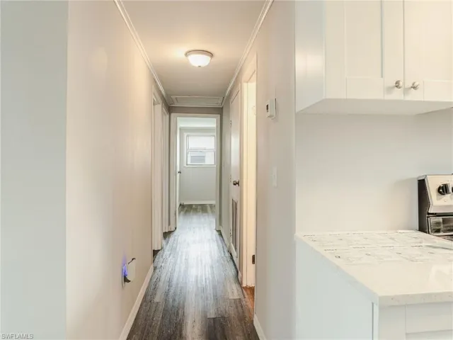Hallway featuring wood-finish flooring, light neutral wall tones, and crown molding