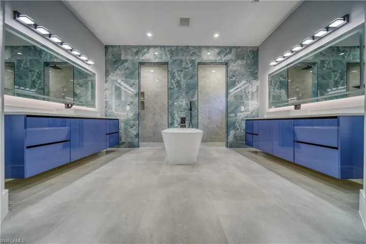 Master bath with a freestanding tub, visible vents, two vanities, and tile walls