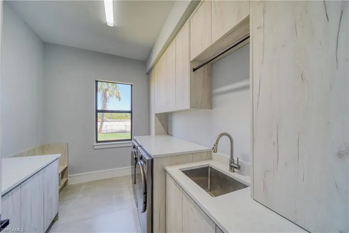Clothes washing area, light tile floors, cabinet space, independent washer and dryer, and a sink