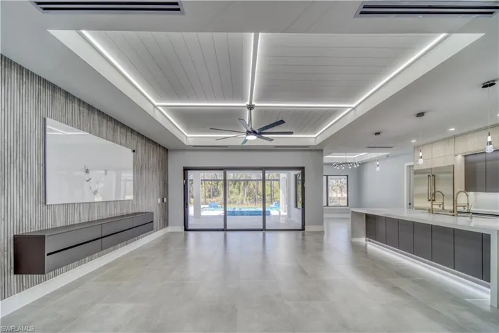 Great room with ceiling fan, LED lights, a tray ceiling, and an TV accent wall