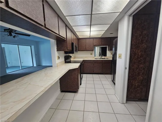 Kitchen featuring ample cabinetry, white tile flooring, light-toned countertops, a built-in oven, and a pass-through counter opening to another room