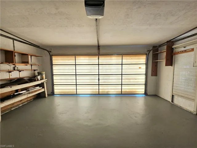 Attached garage with an overhead door, smooth concrete flooring, and built-in shelving