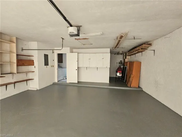 Spacious garage with coated flooring, wall-mounted shelving, built-in cabinetry, and an overhead garage door opener