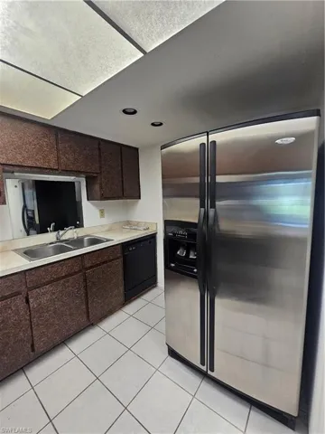 Kitchen featuring brown cabinetry, a stainless steel side-by-side refrigerator, a black dishwasher, a dual basin sink, and ceiling-mounted lighting