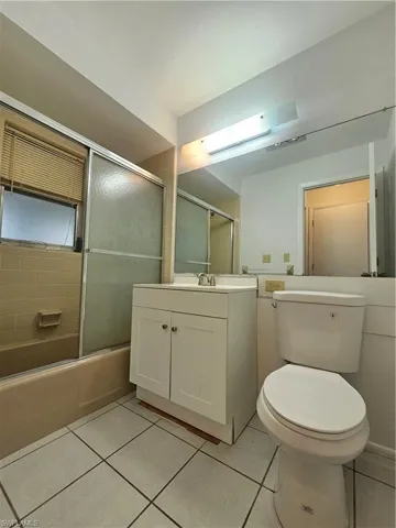 Tile flooring, vanity with storage, mirrored wall, built-in tub with sliding glass enclosure, and wall-mounted lighting fixture