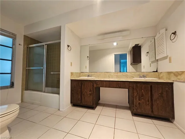 Dual sink vanity with stone-finish countertop, wood-finish cabinetry, and a full-width mirror