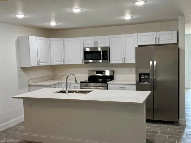 Kitchen with stainless steel appliances, white cabinetry, dark wood-type flooring, and sink