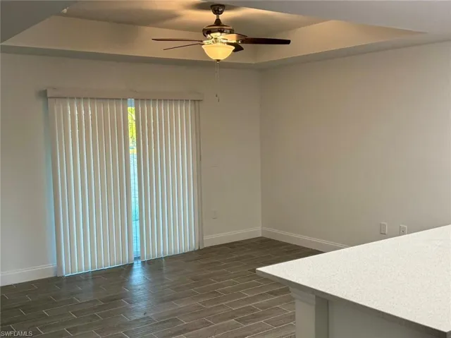 Spare room featuring dark hardwood / wood-style floors, ceiling fan, and a tray ceiling