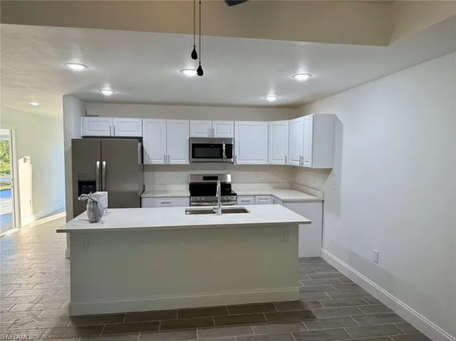 Kitchen featuring stainless steel appliances, white cabinetry, dark hardwood / wood-style floors, and a center island with sink
