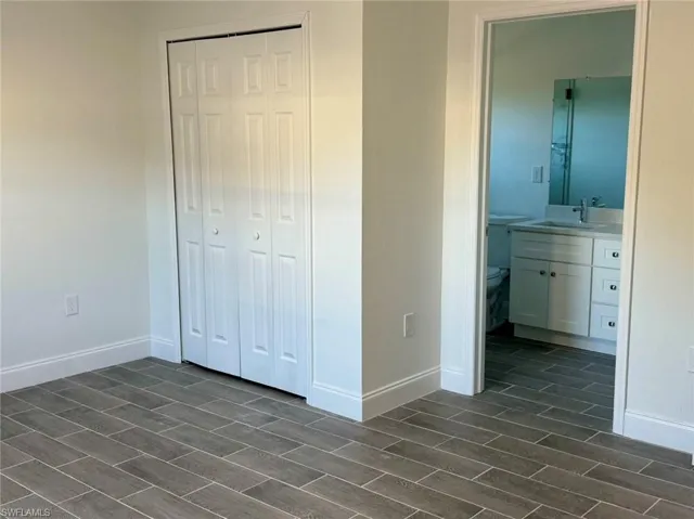 Unfurnished bedroom featuring connected bathroom, a closet, sink, and dark hardwood / wood-style floors