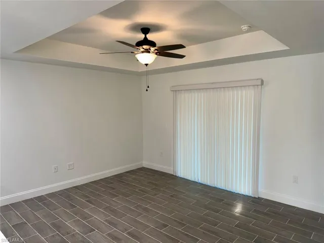 Spare room with a raised ceiling, ceiling fan, and dark wood-type flooring
