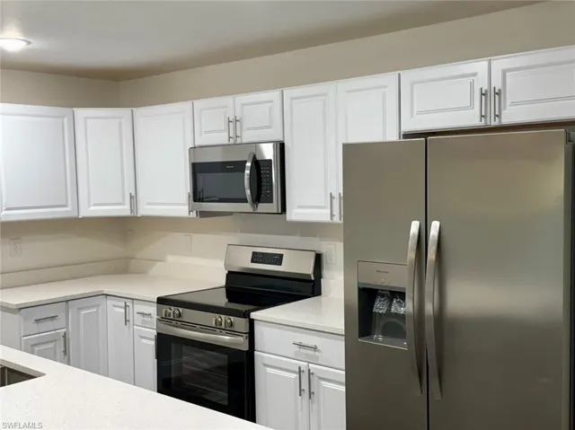 Kitchen featuring stainless steel appliances, white cabinetry, and light stone counters