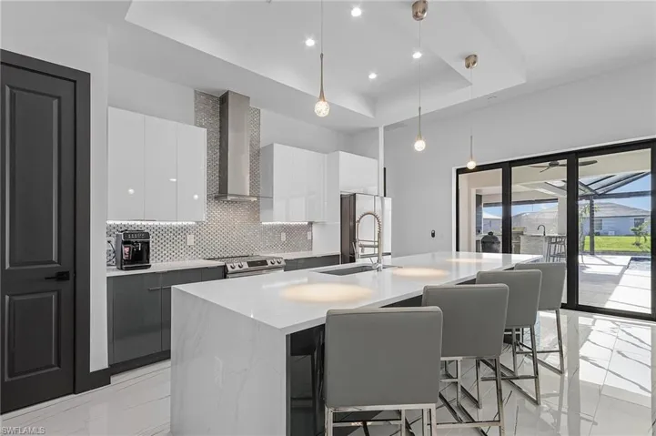 Kitchen with hanging light fixtures, wall chimney exhaust hood, sink, a center island with sink, and a raised ceiling