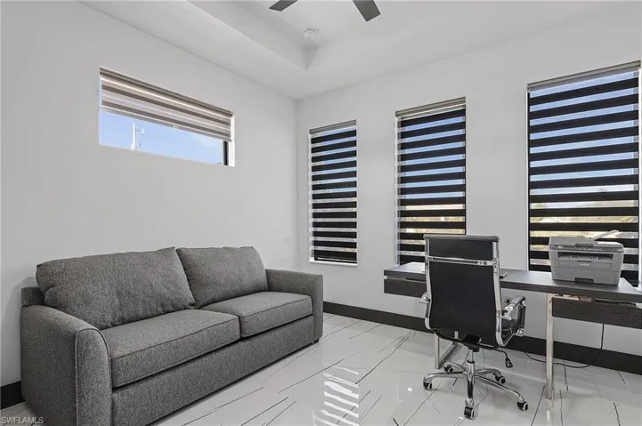Home office with light tile patterned flooring, a raised ceiling, and ceiling fan