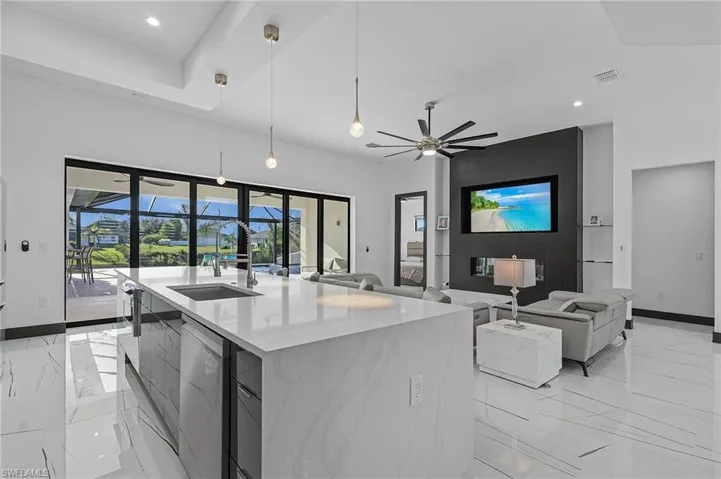 Kitchen featuring decorative light fixtures, ceiling fan, dishwasher, a center island with sink, and light tile patterned floors