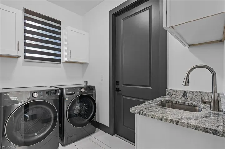Laundry area with separate washer and dryer, cabinets, light tile patterned floors, and sink