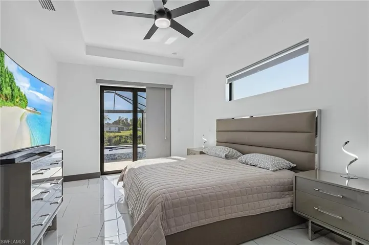 Tiled bedroom featuring access to outside, a raised ceiling, multiple windows, and ceiling fan