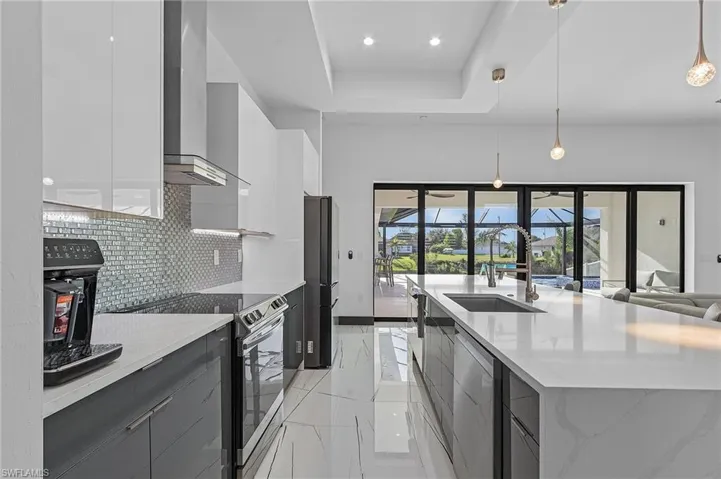 Kitchen featuring pendant lighting, wall chimney exhaust hood, a raised ceiling, appliances with stainless steel finishes, and backsplash