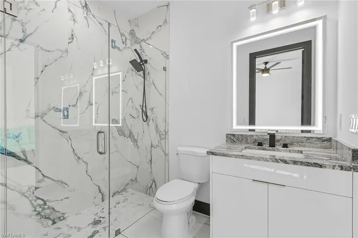 Bathroom with vanity, ceiling fan, an enclosed shower, toilet, and tile patterned flooring