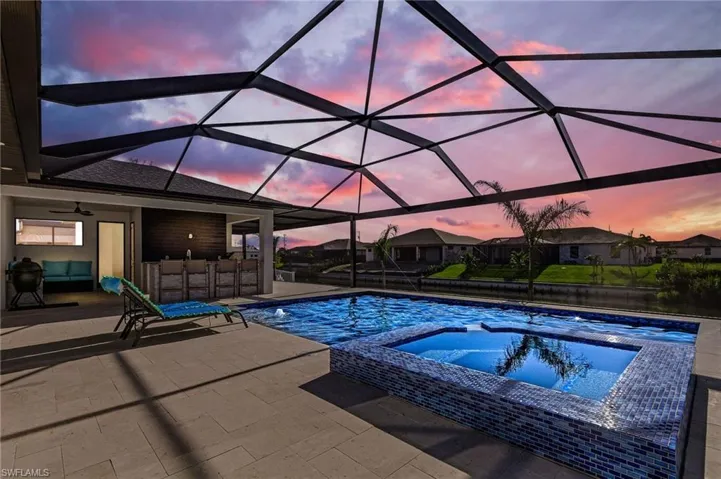 Pool at dusk featuring an in ground hot tub, a patio, glass enclosure, and ceiling fan