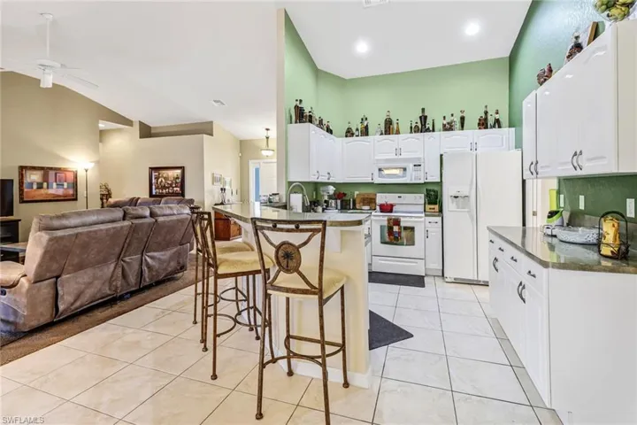 Kitchen featuring a breakfast bar area, vaulted ceiling, light tile patterned flooring, white cabinetry, and white appliances