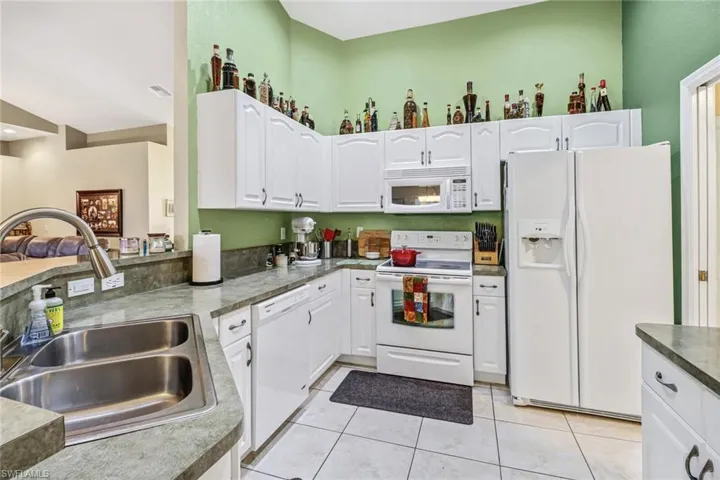 Kitchen with white cabinetry, sink, light tile patterned floors, and white appliances