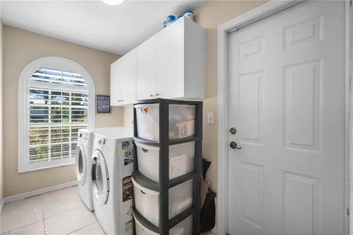 Laundry area featuring light tile patterned floors, cabinet space, and washing machine and clothes dryer