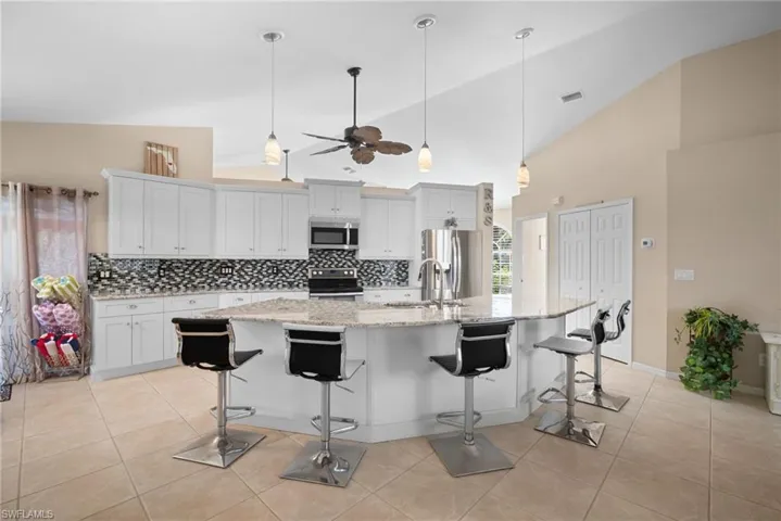 Kitchen with a kitchen breakfast bar, hanging light fixtures, tasteful backsplash, appliances with stainless steel finishes, and high vaulted ceiling