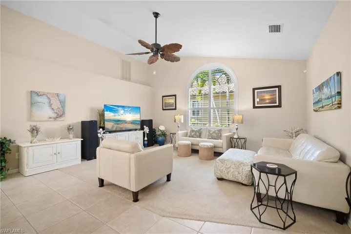Carpeted living room with a ceiling fan, tile patterned flooring, and vaulted ceiling