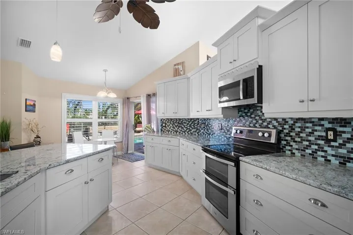 Kitchen with appliances with stainless steel finishes, lofted ceiling, pendant lighting, white cabinetry, and tasteful backsplash