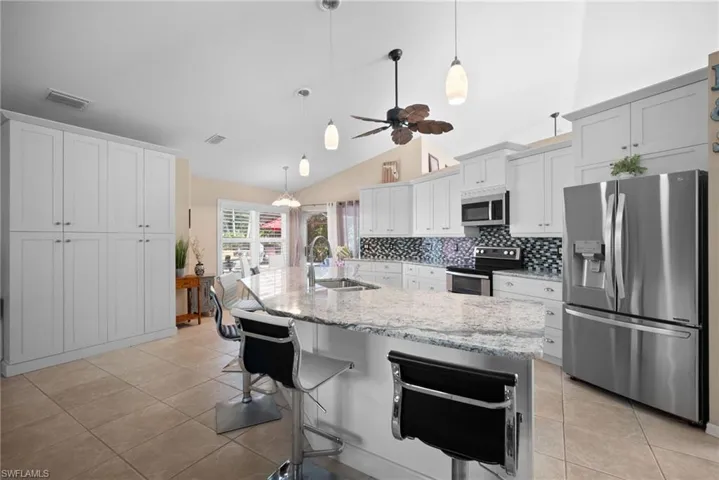 Kitchen featuring stainless steel appliances, a breakfast bar area, decorative backsplash, hanging light fixtures, and light stone counters