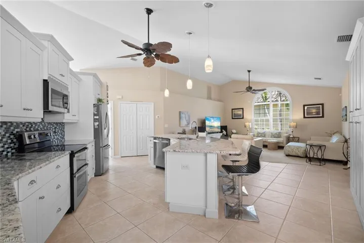 Kitchen with stainless steel appliances, white cabinets, tasteful backsplash, pendant lighting, and high vaulted ceiling