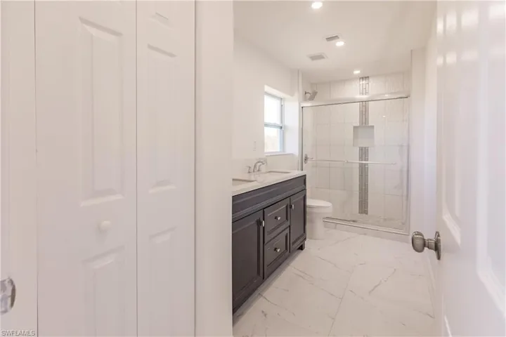 Full bath featuring marble finish floors, a shower stall, double vanity, recessed lighting, and a closet