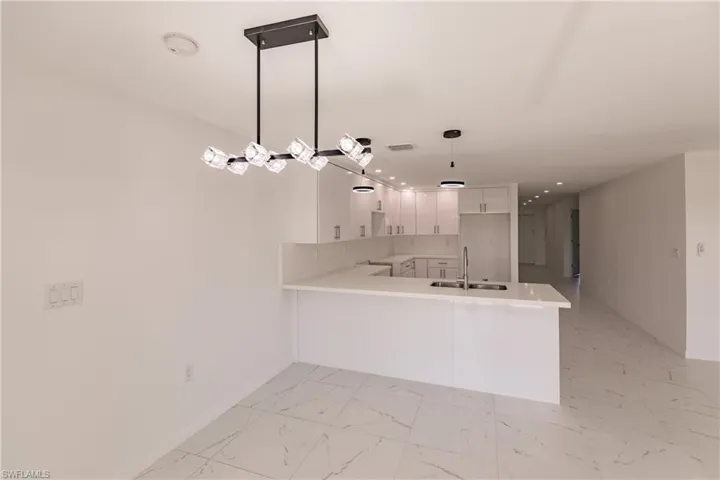 Kitchen with a peninsula, light countertops, white cabinets, light marble finish flooring, and recessed lighting