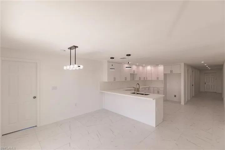 Kitchen featuring a peninsula, recessed lighting, light marble finish flooring, white cabinets, and light countertops