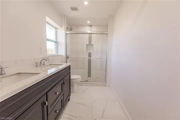 Bathroom with marble finish flooring, a stall shower, recessed lighting, and double vanity
