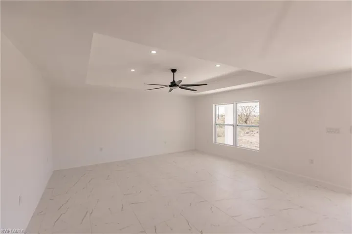 Unfurnished room with a raised ceiling, recessed lighting, a ceiling fan, and light marble finish flooring