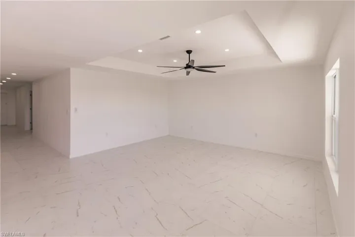Spare room featuring a tray ceiling, recessed lighting, a ceiling fan, and light marble finish flooring