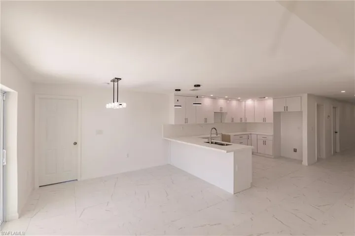 Kitchen featuring a peninsula, recessed lighting, light marble finish floors, white cabinets, and light countertops