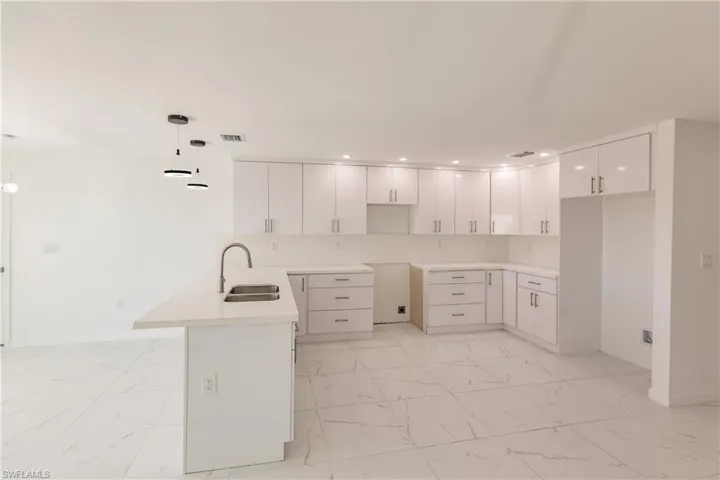 Kitchen featuring light marble finish flooring, a peninsula, recessed lighting, white cabinets, and decorative light fixtures