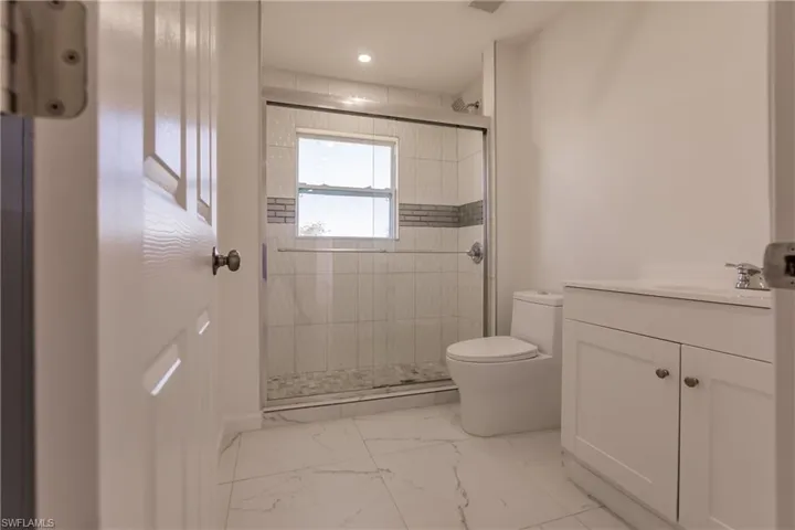 Full bathroom with vanity, a shower stall, marble look tiles, and recessed lighting