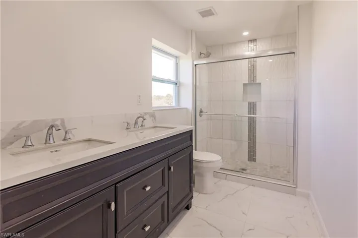 Bathroom with marble finish floors, a shower stall, double vanity, and recessed lighting