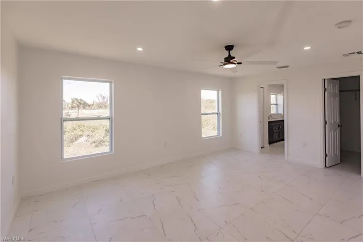 Unfurnished bedroom with recessed lighting, light marble finish flooring, ensuite bathroom, a walk in closet, and ceiling fan