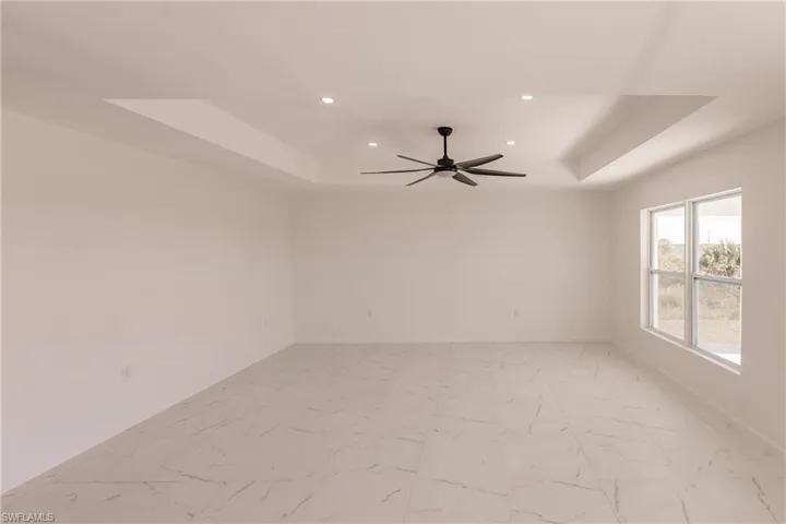 Empty room featuring a raised ceiling, recessed lighting, ceiling fan, and light marble finish floors