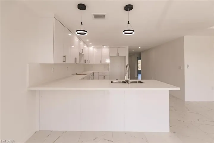 Kitchen featuring light marble finish floors, a peninsula, white cabinetry, light countertops, and recessed lighting
