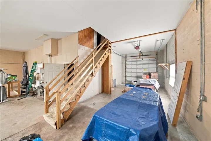 Multi-use garage area featuring concrete flooring, exposed masonry walls, a sectional overhead door, and an integrated wooden staircase providing access to an upper level