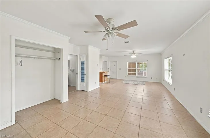 Open-concept interior featuring large-format ceramic tile flooring, two ceiling fans, multi-paned windows, and a built-in reach-in closet