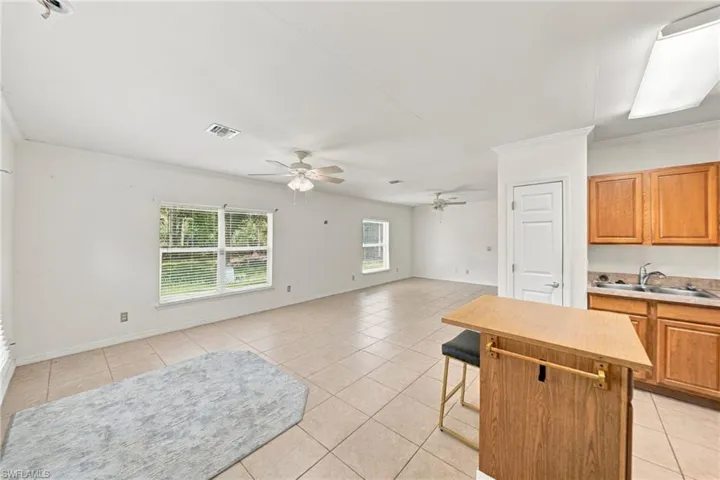 Open-concept living space featuring ceramic tile flooring, dual ceiling fans, light wood-finish cabinetry, and a kitchen island