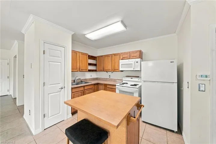 Kitchen featuring wood cabinetry, laminate countertops, a dual-basin stainless steel sink, tile flooring, and built-in appliances including an over-the-range microwave